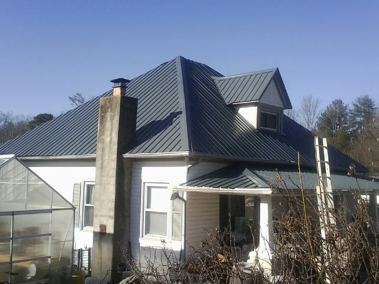 Dark blue standing seam metal roof on a white farmhouse with dormer — Slate & Tile Roof Repair by Roofing Brothers in Dripping Springs