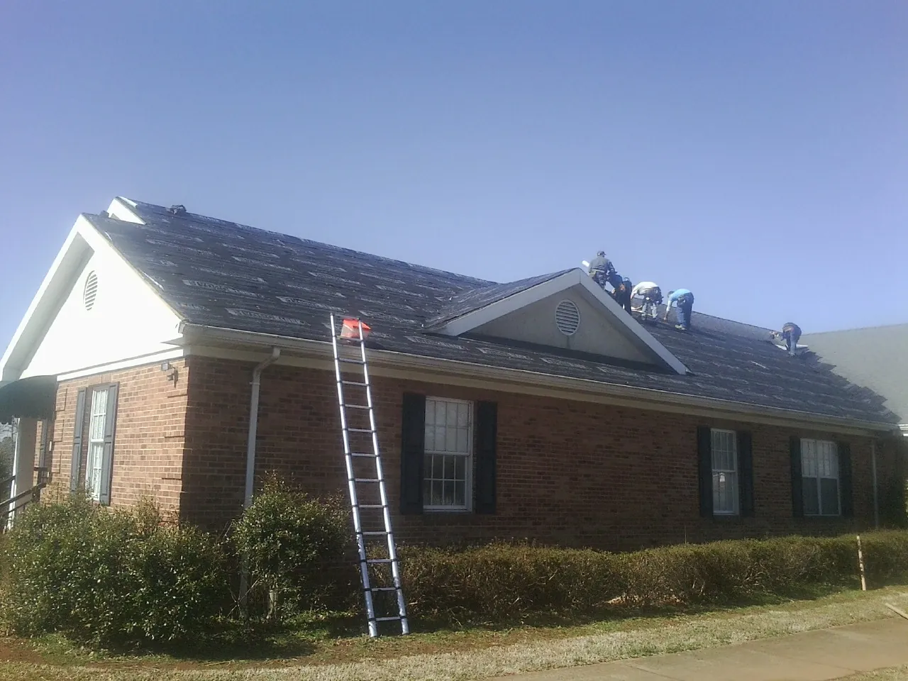 Crew tearing shingles off a brick ranch roof with a ladder set — Metal Roof Repair work by our crew in Dripping Springs