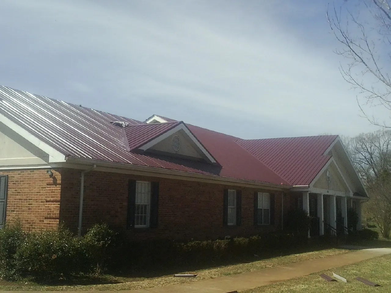 Red metal roof with gabled entries on a long brick building, from a Hail Damage Roof Repair job in Dripping Springs