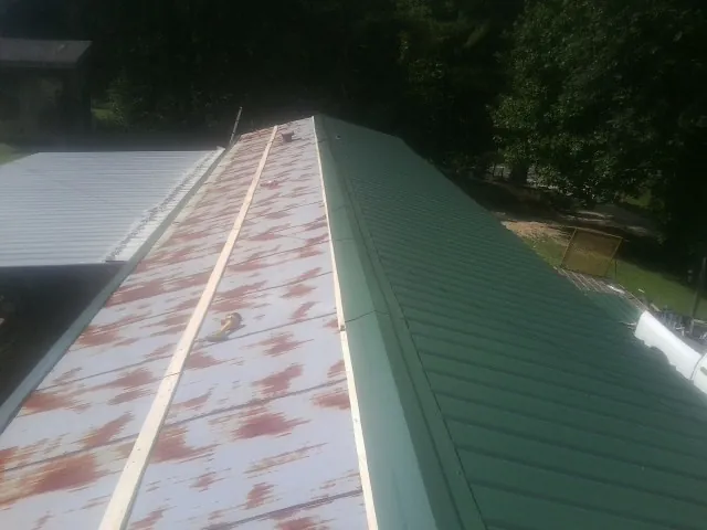 Old rusted panels beside newly installed green metal roofing — Wind Damage Roof Repair by Roofing Brothers in Dripping Springs