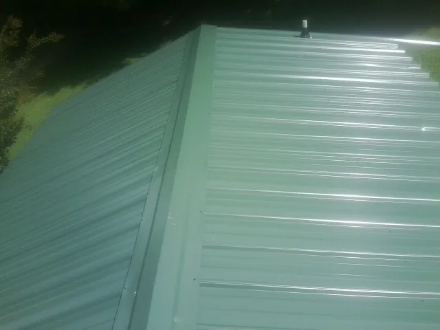 New green metal panels meeting at the ridge of a roof — Flat Roof Repair work by our crew in Dripping Springs