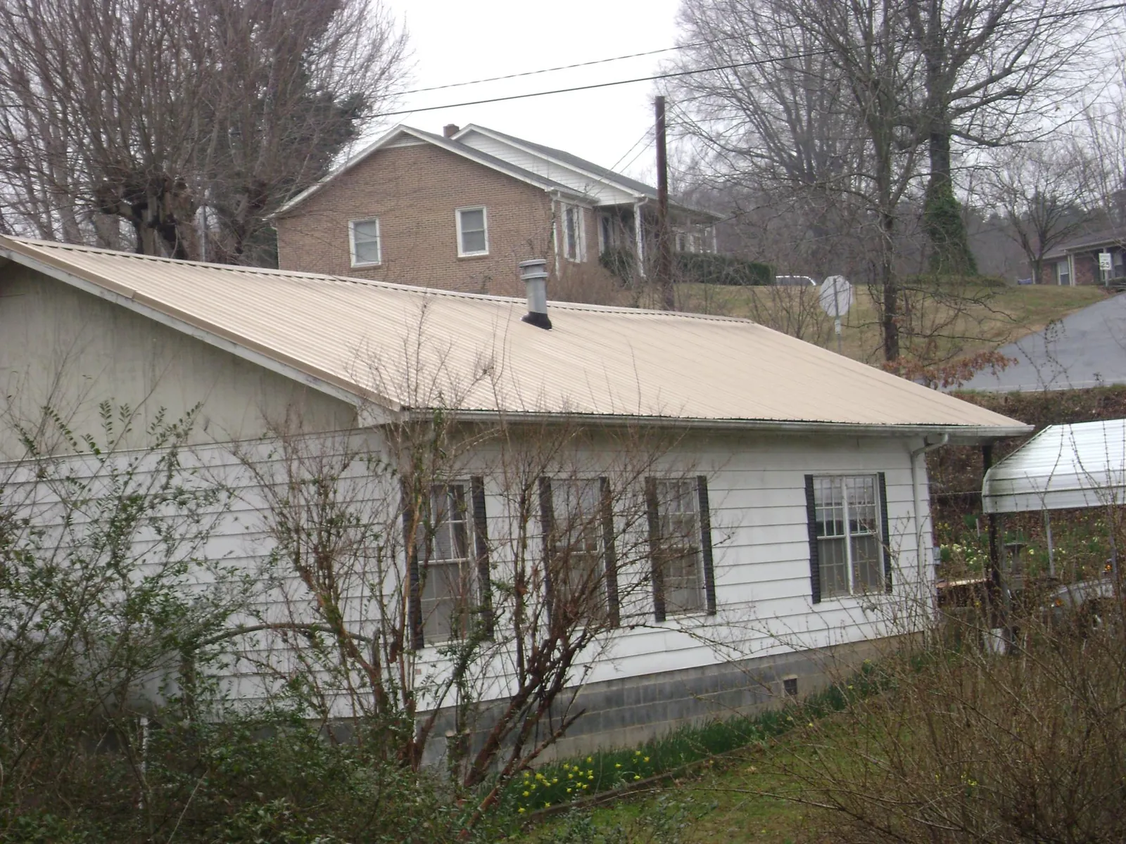Tan metal roof on a white sided house set into a hillside — Commercial Roofing by Roofing Brothers in Dripping Springs