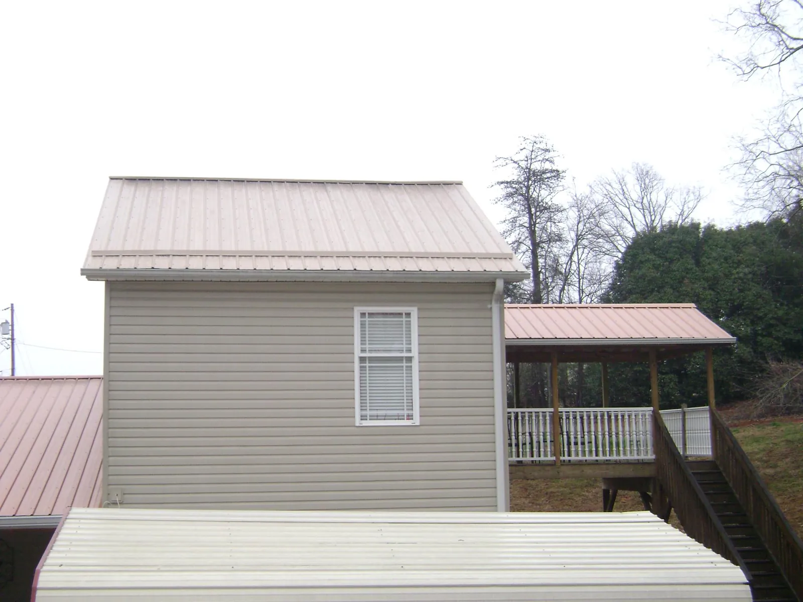 Tan metal roofs on a two story addition and attached porch, from a Roof Replacement job in Dripping Springs